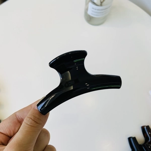 Close-up of a minimalist glossy black hair claw clip held by hand against a white background