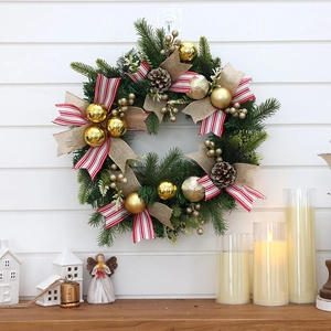 Artificial Christmas wreath with gold baubles, pine cones, and bows on a white wall