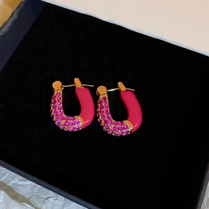Macro view of U-shaped gold earrings with pink enamel and fuchsia zircon inlay