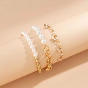 Close-up of pearl and gold chain bracelet set displayed on a warm pink cylinder