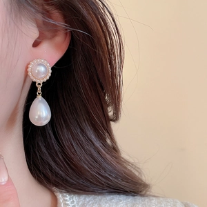 Detail of elegant pearl drop earring with golden base and clusters on a model