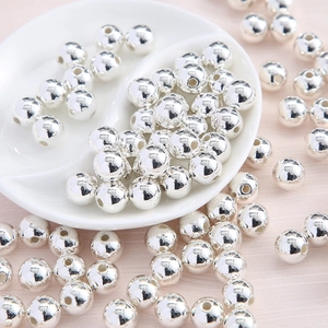 Macro shot of silver-plated acrylic round beads for DIY jewelry making in a white ceramic bowl