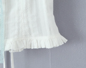 Detailed close-up of white textured fabric featuring vertical stripes and ruffled hem
