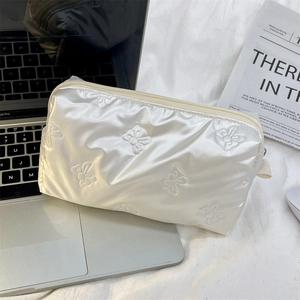 Detailed view of white quilted butterfly pattern makeup bag next to a laptop on white fabric