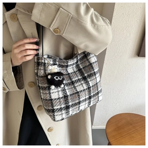 Nahaufnahme der schwarz-weißen Tweed-Einkaufstasche mit Anhänger am Model in beige