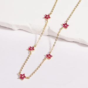 Close-up of golden necklace featuring red floral charms with sparkling crystal centers