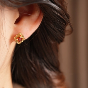 Close-up of vintage gold stud earring with red zircon inlay on person's ear