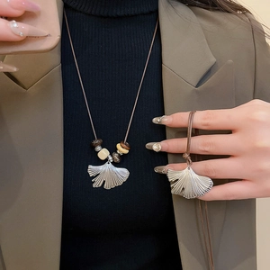 Detail of silver ginkgo leaf pendant on brown braided cord with wooden beads necklace