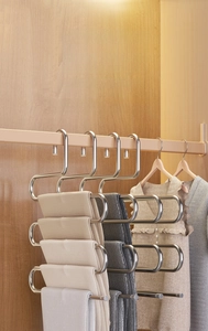 Detail view of S-shaped stainless steel multi-layer pants hanger in a wooden wardrobe