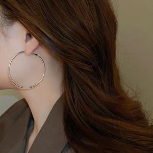 Macro view of large silver hoop earring worn by a model showcasing its size and polish