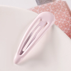 Close-up of a light pink glossy snap hair clip on a white ceramic plate backdrop