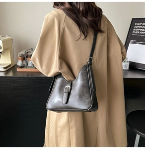 Détail du sac seau rétro gris foncé avec surpiqûres et boucle argentée sur un trench-coat