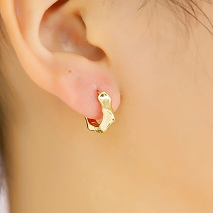 Gros plan d'une boucle d'oreille géométrique irrégulière dorée au style métal minimaliste