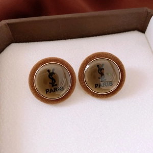 Close-up of retro brown velvet earrings with amber dome and centered gold logo detail