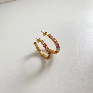 Detailed close-up of golden hoop earrings with multi-colored square zircon stones on a white background