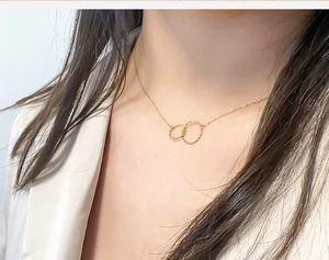 Detail of double ring titanium necklace with hammered gold texture on female neck