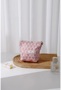 Pink heart-textured makeup bag with a 3D floral zipper pull on a wooden tray