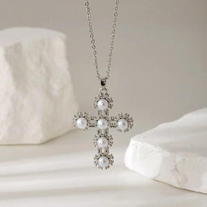 Elegant silver cross necklace with inlaid white pearls on a minimalist stone display