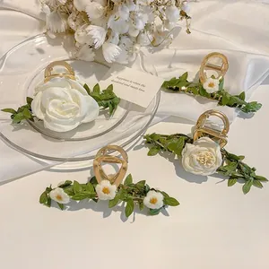Detail of golden metal hair claw clips with white roses and green leaf decorations