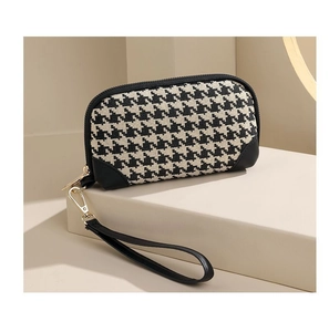 Detail of houndstooth clutch bag featuring black leather trim and detachable wristlet strap