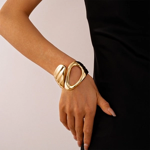 Detail shot of a polished gold geometric hollow cuff bracelet on a model's wrist
