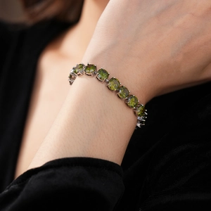 Detailed view of an olive green round cut zircon tennis bracelet on a female wrist