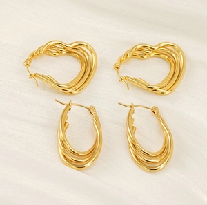 Macro detail of multi-layered 18K gold heart and oval hoop earrings on white fabric