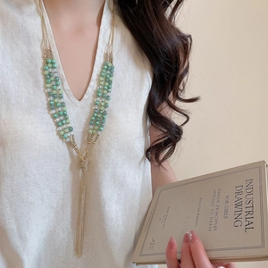 Detail of layered beaded necklace with green gradient crystals and golden tassels
