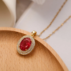 Gold plated necklace featuring an oval pendant with a red gemstone and crystal halo