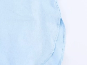 Detail view of the curved hem and side slit design on a light blue linen shirt