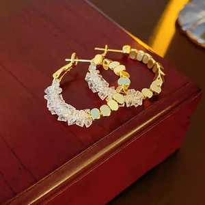 Détail macro de créoles plaquées or avec perles de cristal sur un coffret en bois