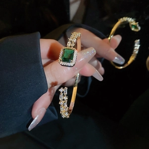 Close-up of square emerald gemstone and white crystals on a gold open cuff bracelet