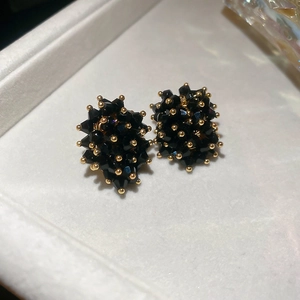 Macro shot of irregular black crystal stud earrings with gold bead accents on white tray