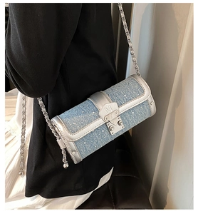Detail of a denim blue cylindrical crossbody bag with silver trim and metallic M buckle