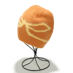 Close-up of warm orange plush knitted beanie featuring a yellow bow jacquard pattern