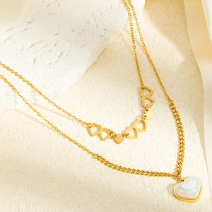 Détail d'un collier doré multicouche avec breloques cœur et pendentif nacré sur pierre