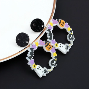 Détail de boucles d'oreilles Halloween en acrylique avec citrouilles et fantômes sur plateau céramique