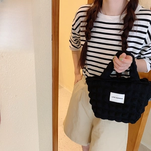 Close-up of black bubble textured handbag with a white label in an outdoor cafe setting