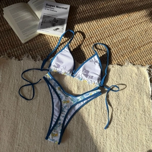 Detailed flat lay of floral bikini set with blue straps on a textured woven mat