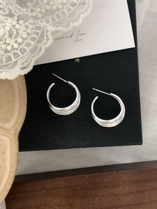 Close-up of silver C-shaped multi-layer earrings with woven texture on a black jewelry box