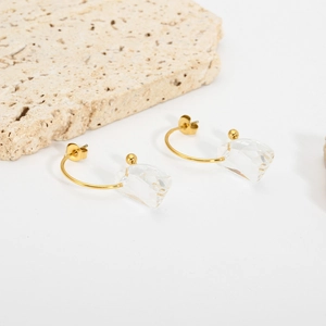 Detail of gold C-shaped earrings with irregular transparent crystals on stone