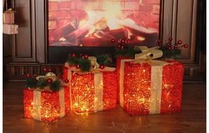 Three-piece red Christmas lighted gift boxes with golden ribbons near a warm fireplace