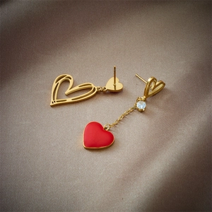Boucles d'oreilles cœur asymétriques dorées avec pendentif rouge sur du satin champagne