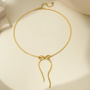 Detail of gold snake bone bracelet featuring a bow charm and lobster clasp