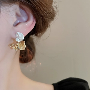 Close-up of elegant gold and silver floral earrings with pearl on a female model