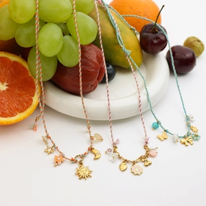 Detail of colorful woven rope necklaces with metal charms displayed on a white plate