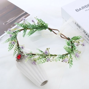 Detail of floral crown with green leaves, purple flowers and a red teardrop pendant