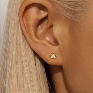 Macro shot of a golden clover stud earring with sparkling white crystals on a model's ear