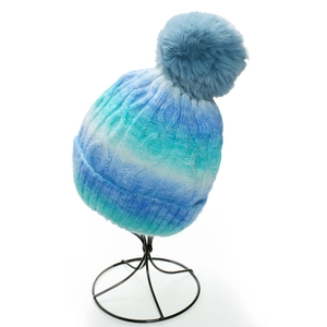 Detail of cable knit winter hat featuring blue tie-dye gradient and large faux fur pompom
