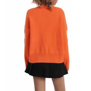 Back view of orange knit sweater paired with black pleated skirt on a model
